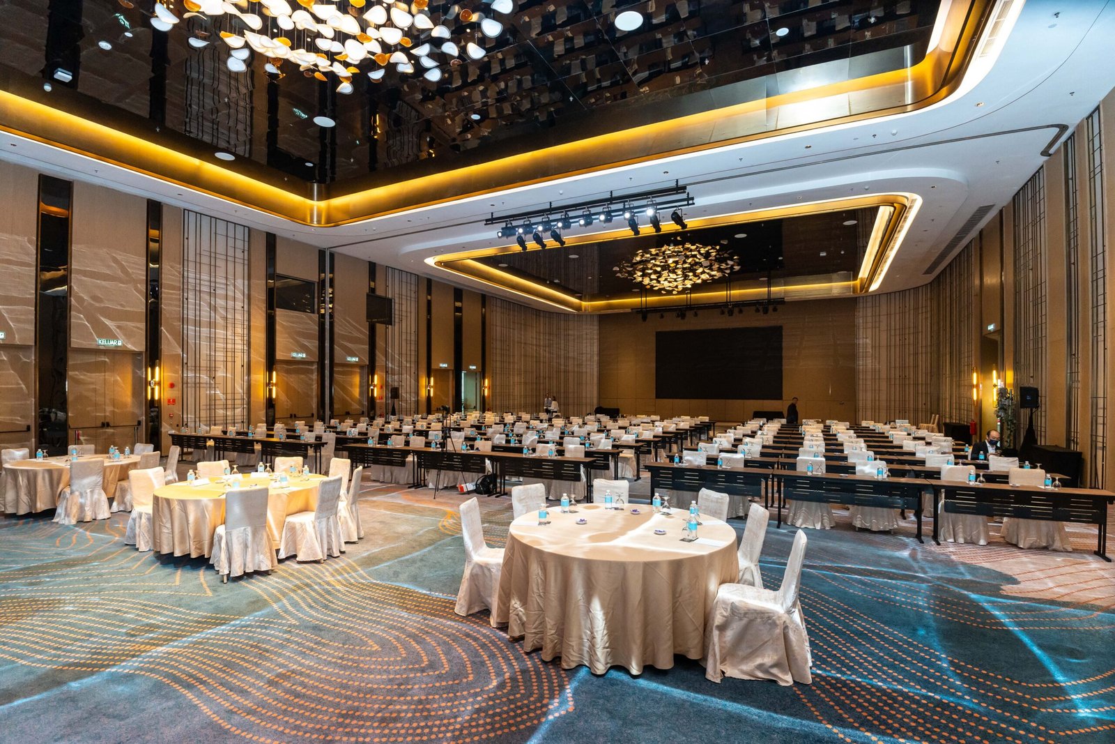 Elegant ballroom setup with round tables, theater-style seating, and sophisticated gold-accented ceiling lighting before
