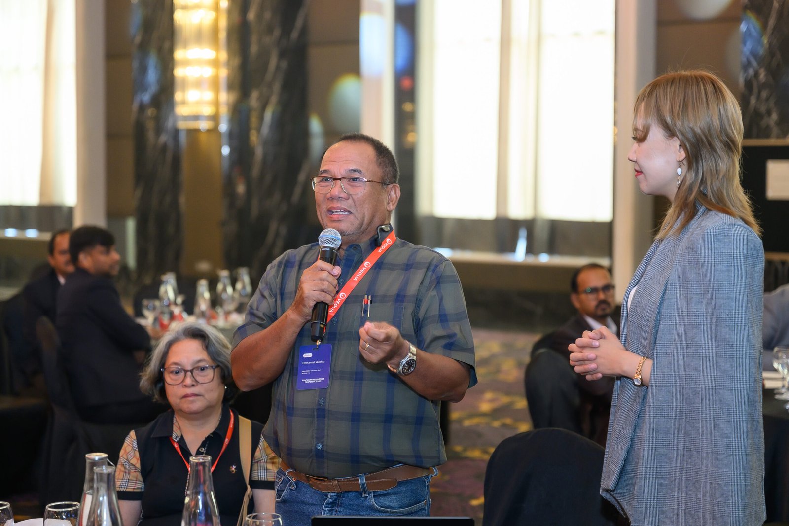 Speaker with microphone engaging in panel discussion at corporate conference with attendees seated at tables